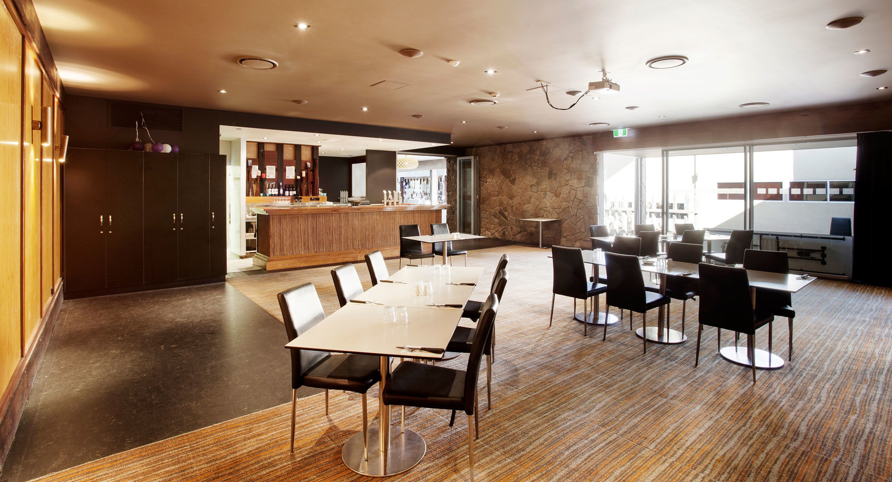 A modern hotel lobby with a bar area, a large seating area with tables and chairs, and a stone accent wall.