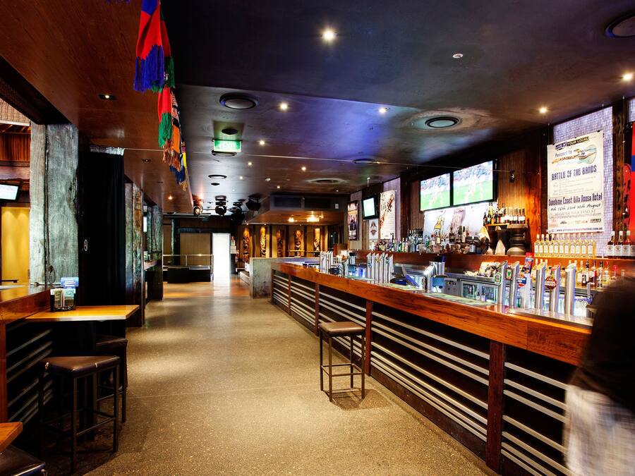 Um bar com mobiliário de madeira, um balcão com diversos frascos e uma tela de televisão exibindo um evento esportivo.