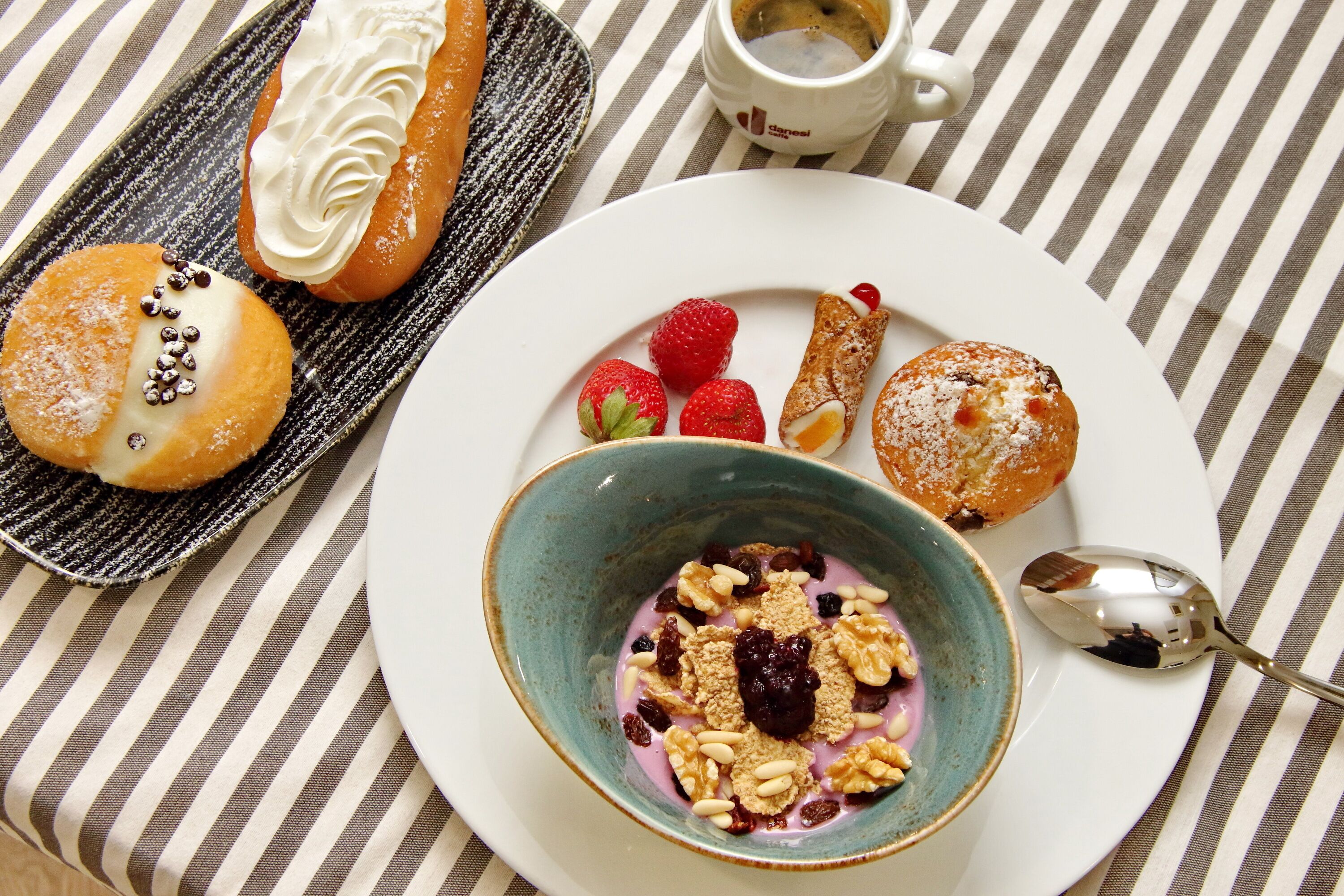 A breakfast setting with pastries, strawberries, and a bowl of yogurt with granola and raisins.
