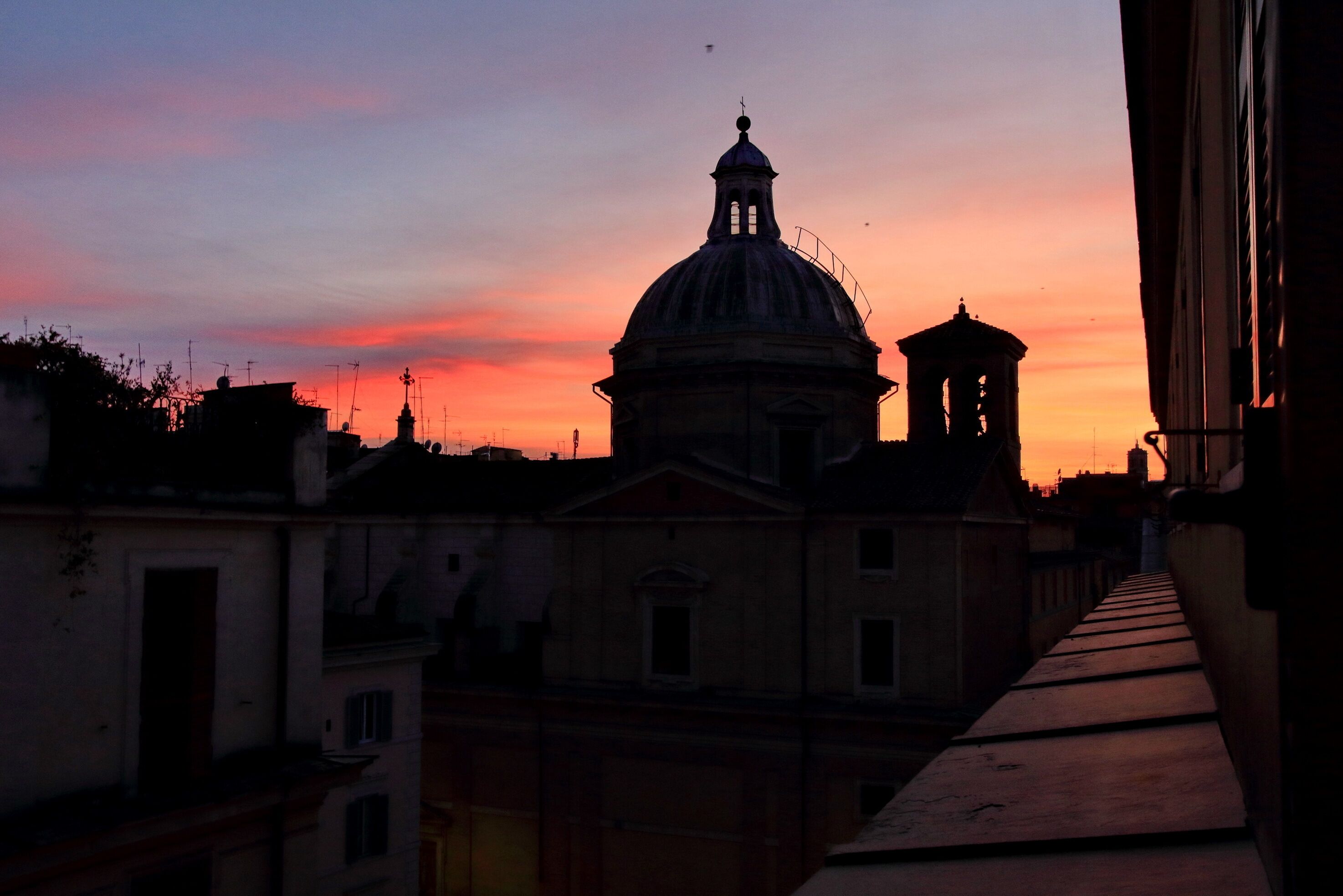 A view of a building with a dome and a bell tower during sunset.