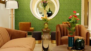 A modern living room with a green patterned wall, a round mirror, and two vases with flowers. - Casa Santa Sofia Hotel (Rome)