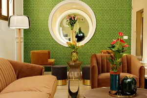 A modern living room with a green patterned wall, a round mirror, and two vases with flowers.