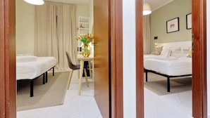 A hotel room with two beds, a desk with a chair, a vase with flowers, and a hanging light fixture. - Casa Santa Sofia Hotel (Rome)