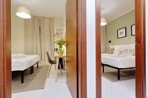 A hotel room with two beds, a small table with a vase of flowers, a chair, and a desk.