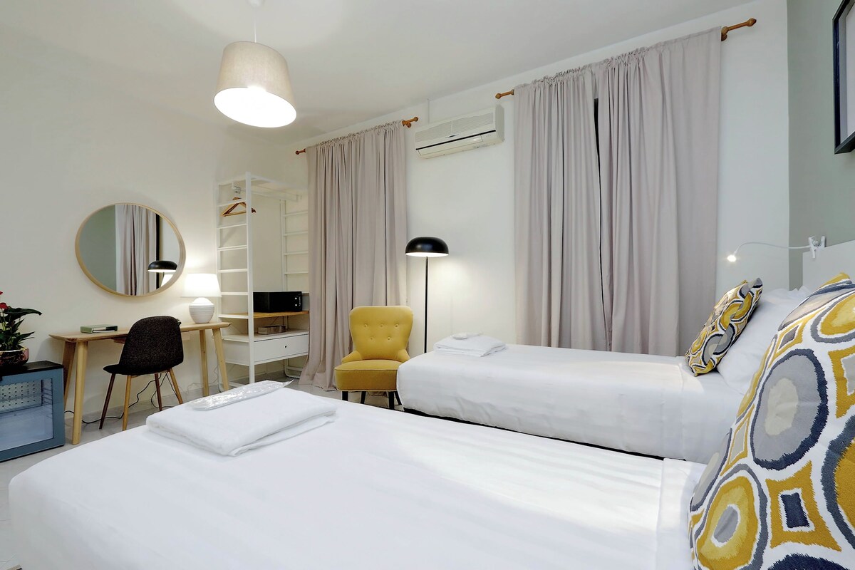 A hotel room with two beds, a desk, a chair, a mirror, and an air conditioning unit.