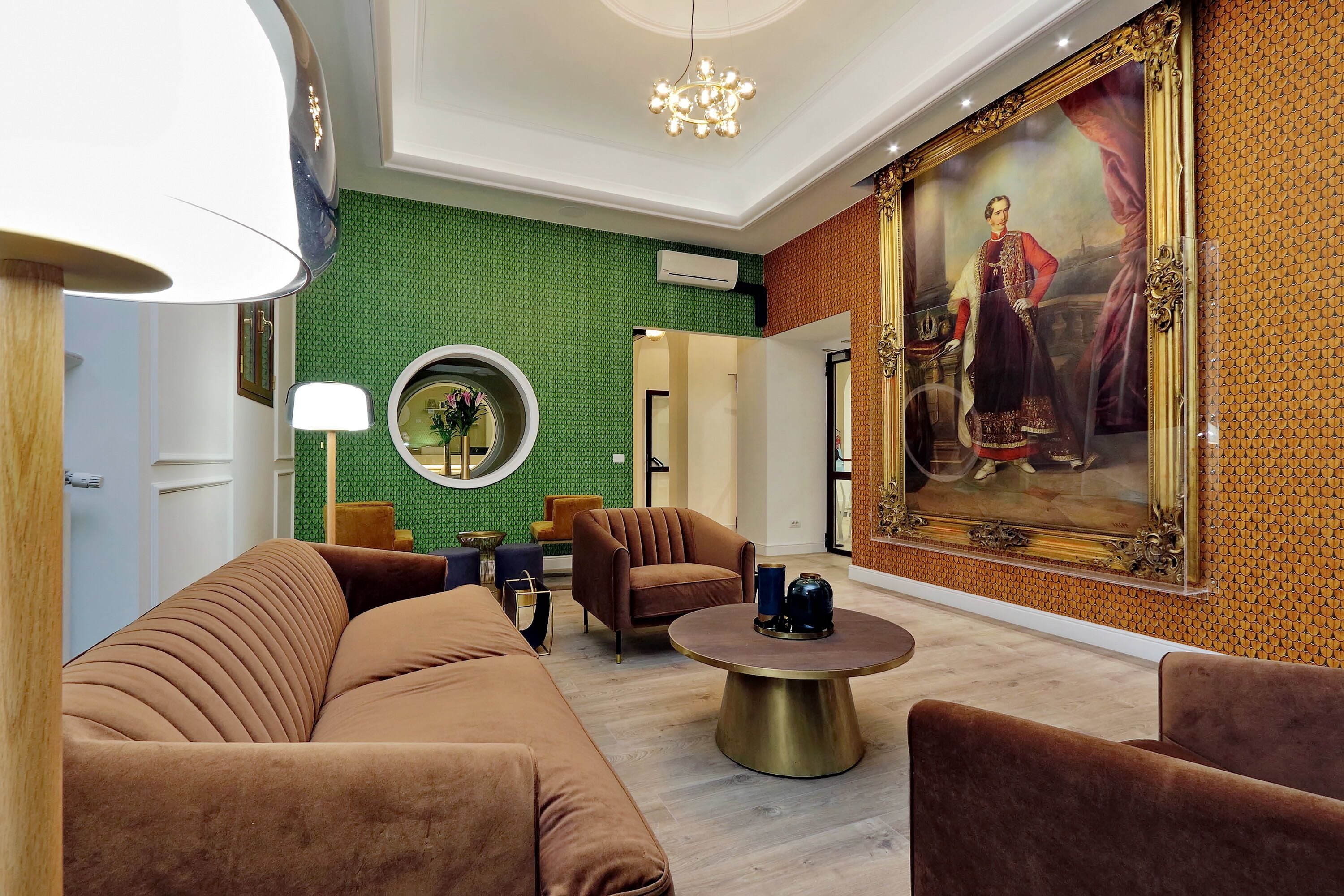 Eine moderne Lobby mit Wand in Grün-Musteroptik, einem großen Porträt und einem runden Spiegel.