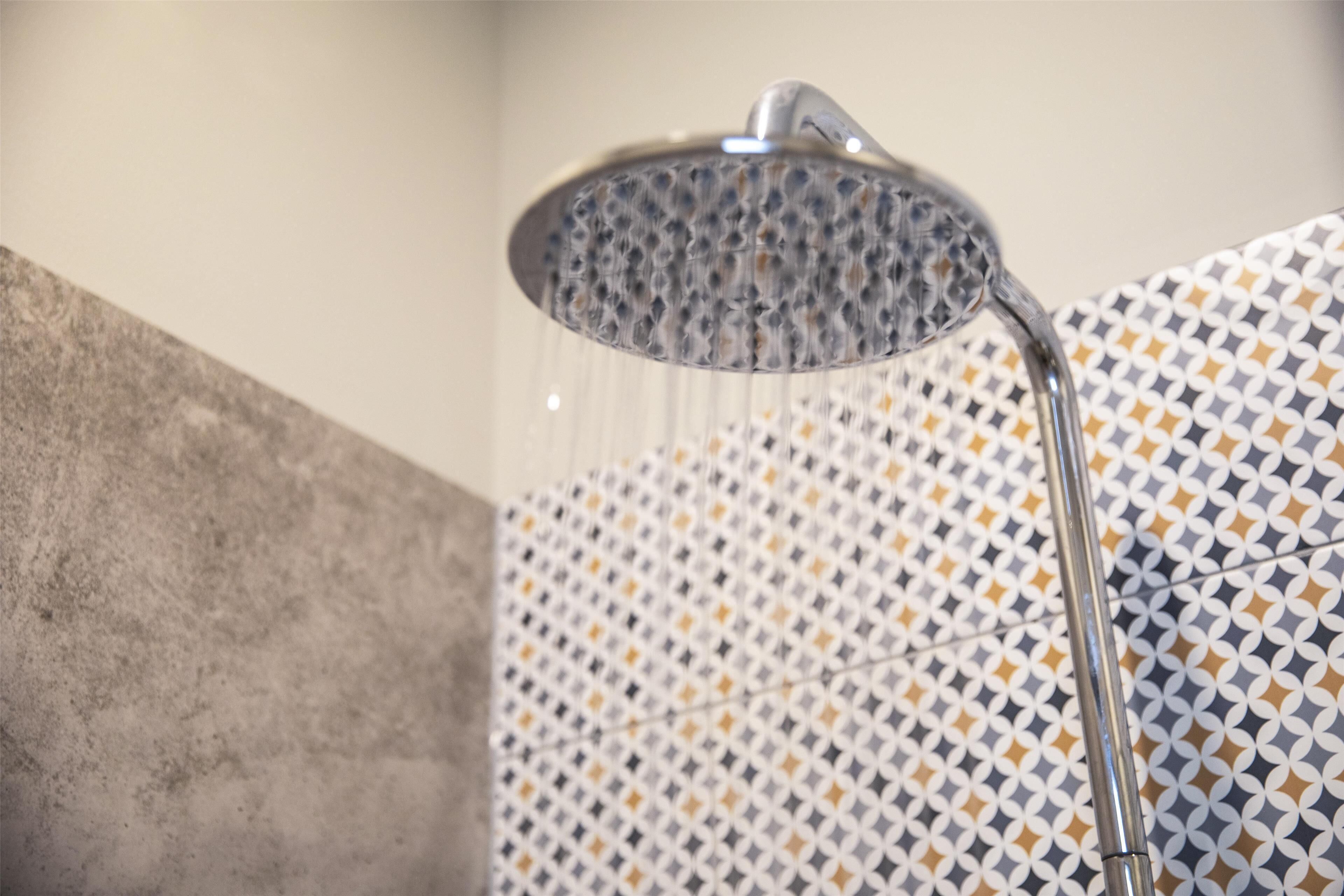 A showerhead with water running, a tiled wall with a geometric pattern, and a concrete ledge.