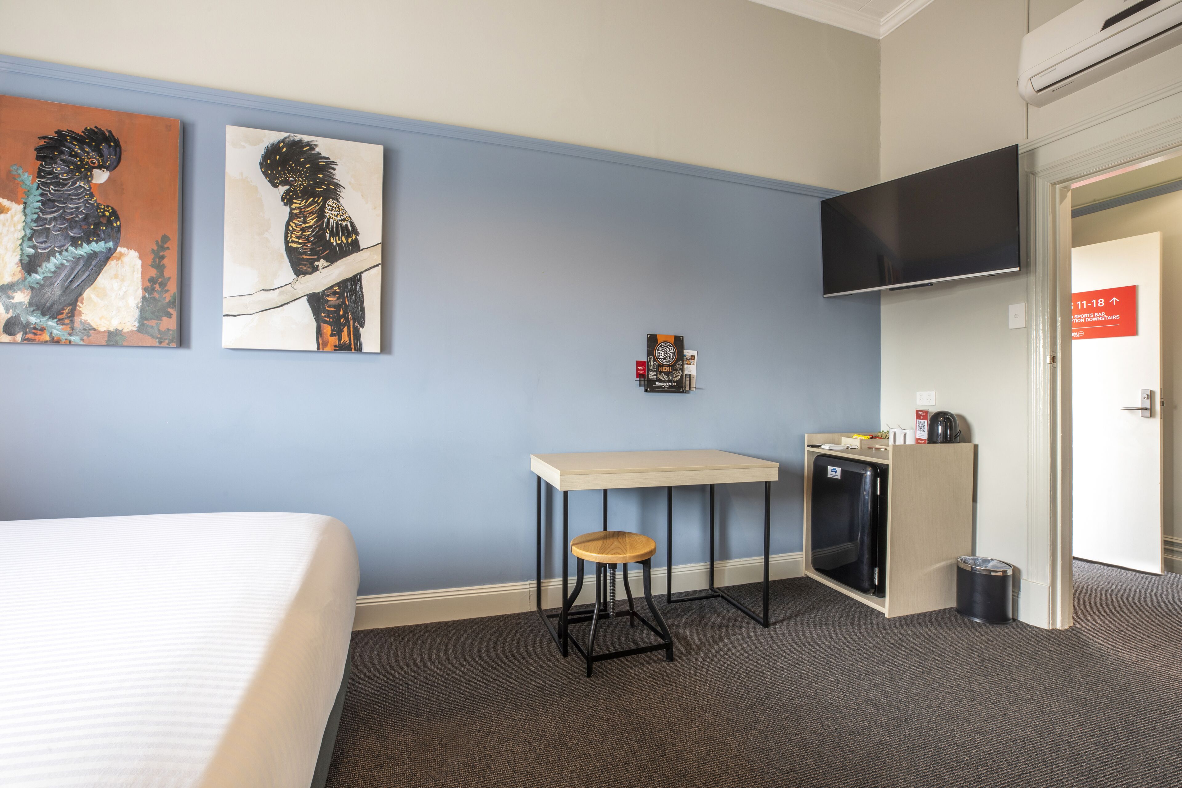 A hotel room with a bed, a desk with a stool, a television, and artwork on the wall.