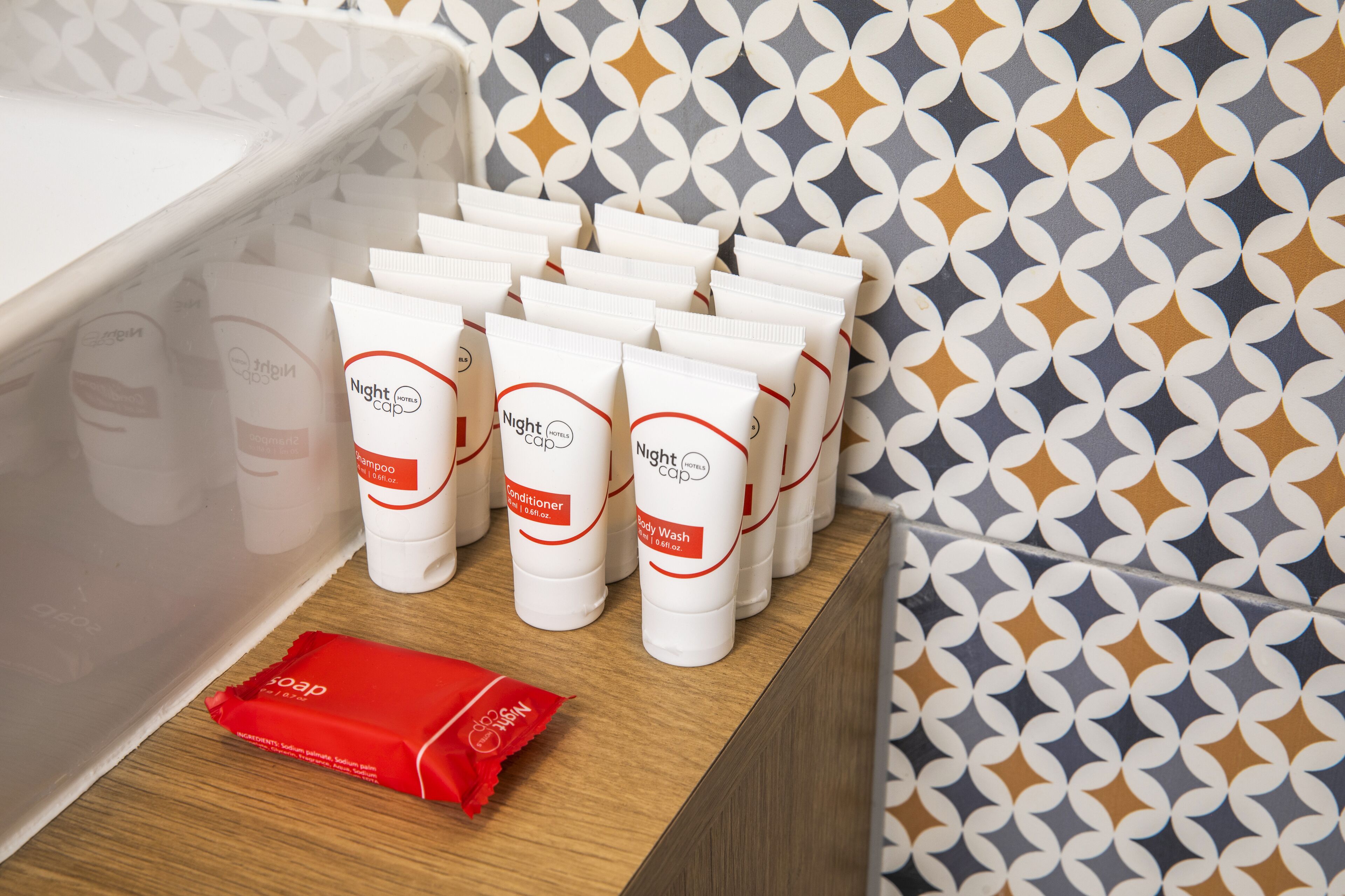 Un bagno con una vasca da bagno bianca, una mensola in legno con diversi prodotti Nightcap e una parete decorata sullo sfondo.