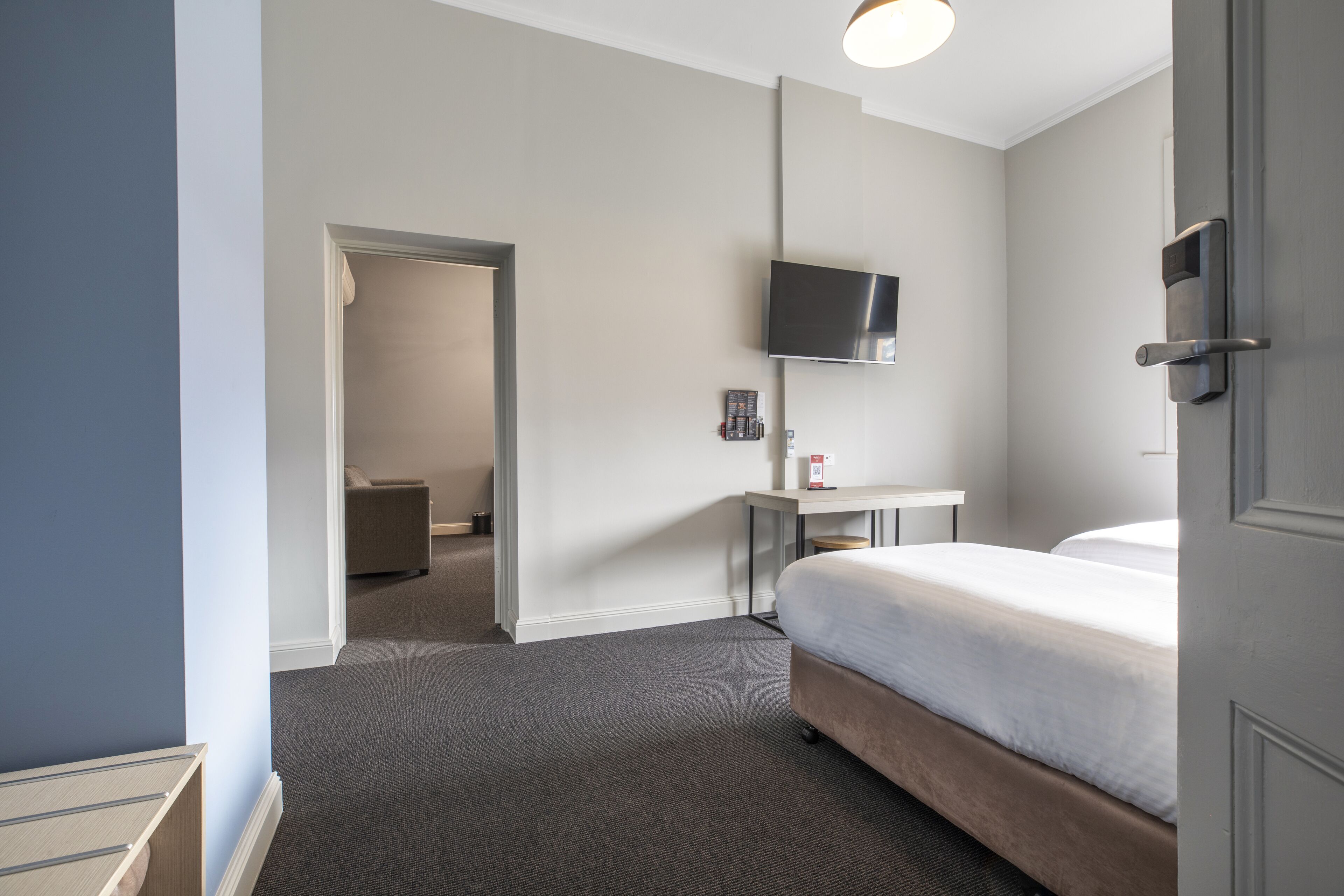 Een hotelkamer met een bed, een bureau, een flatscreen-televisie en een deur.