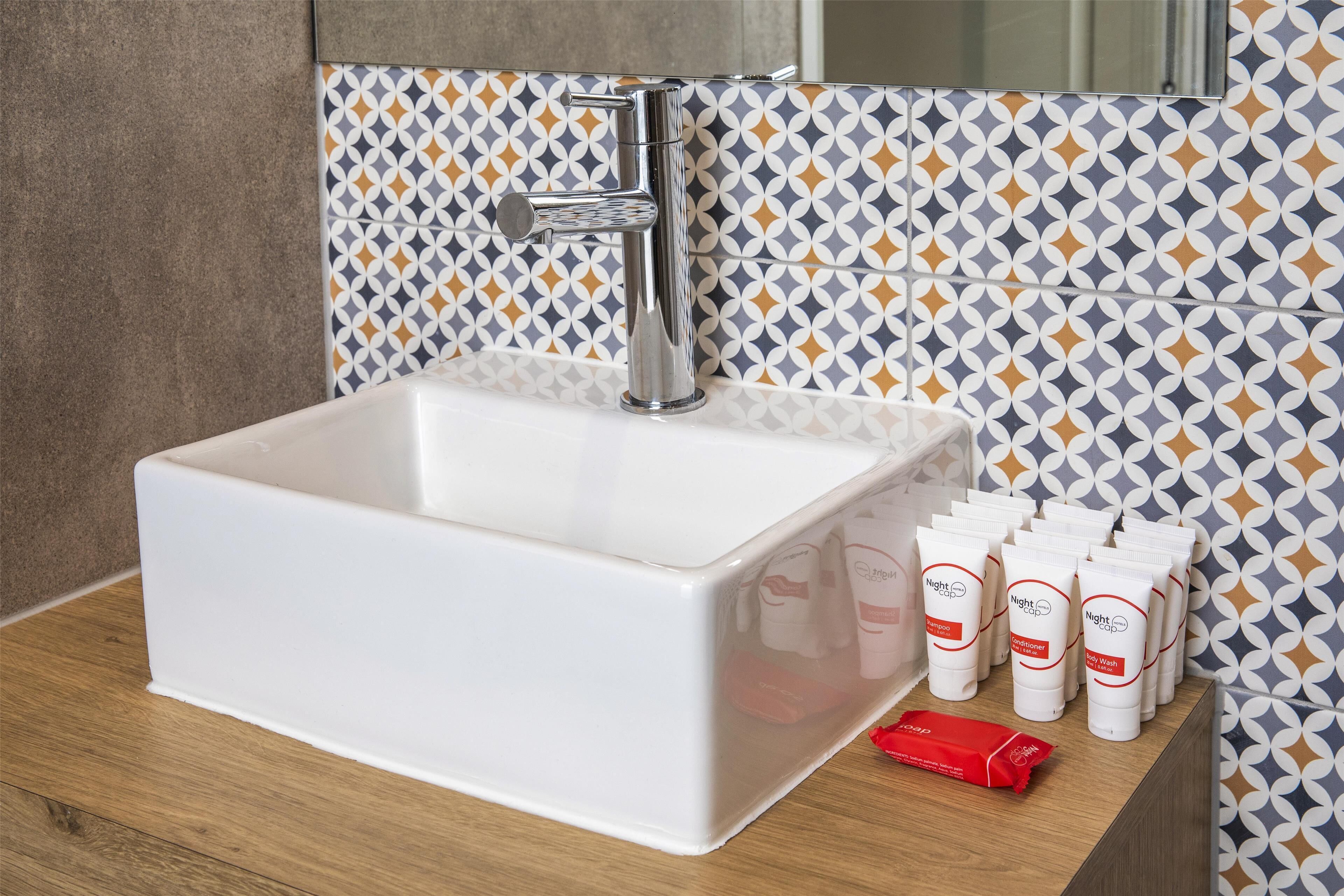 A bathroom with a white sink, chrome faucet, and patterned tiles.
