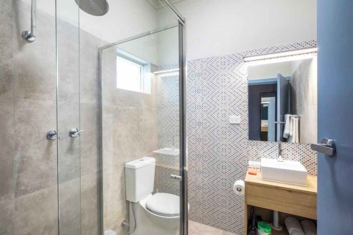 A modern bathroom with a glass shower enclosure, a toilet, and a sink with a mirror above it.