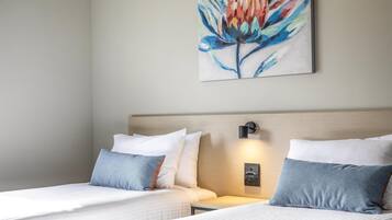 A hotel room with two beds, a nightstand, a wall-mounted lamp, and a painting of a flower.