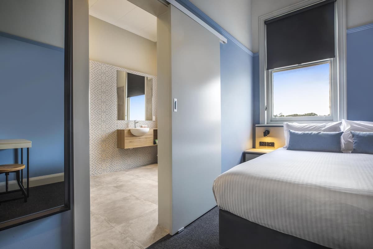Un dormitorio moderno con cama, mesita de noche y baño con lavabo y espejo.