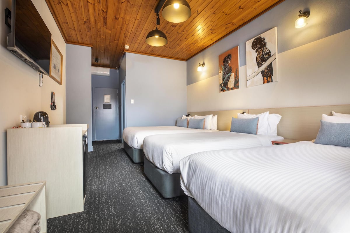 Habitación de hotel con tres camas, un escritorio y techo de madera.