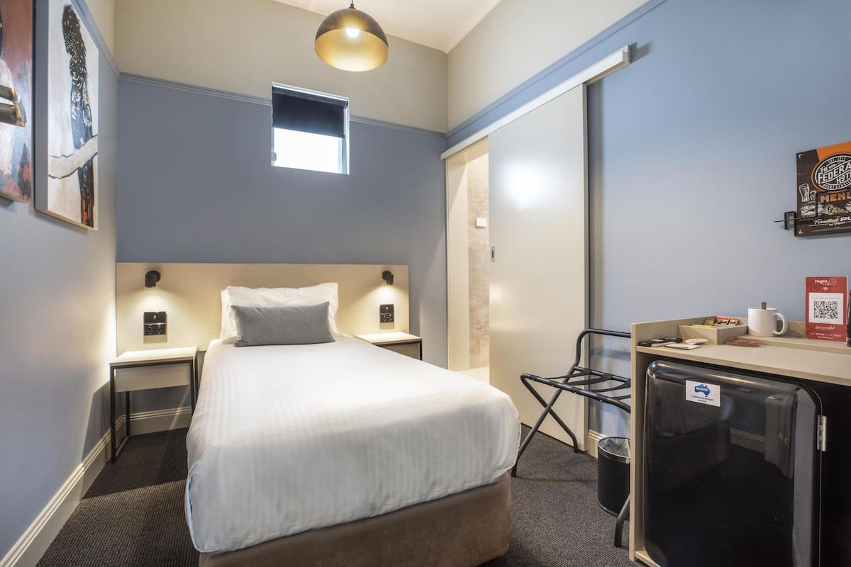 Habitación de hotel con cama, mesitas de noche, escritorio con silla, refrigerador y ventana.