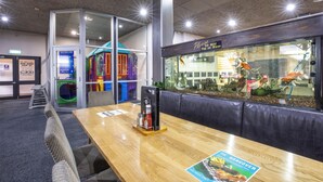 A restaurant with a glass aquarium wall, a children's play area, and a wooden table with a menu.