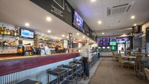A bar with a red counter, multiple stools, and a variety of liquor bottles.