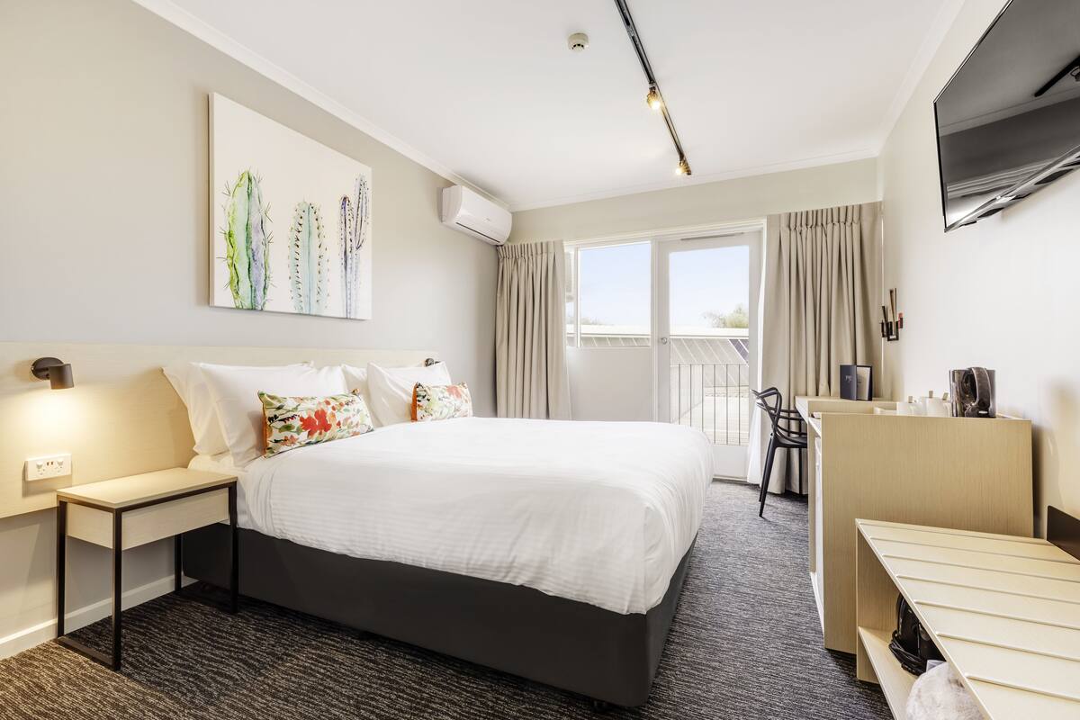 A hotel room with a large bed, a desk, a chair, a TV, and a window with curtains.