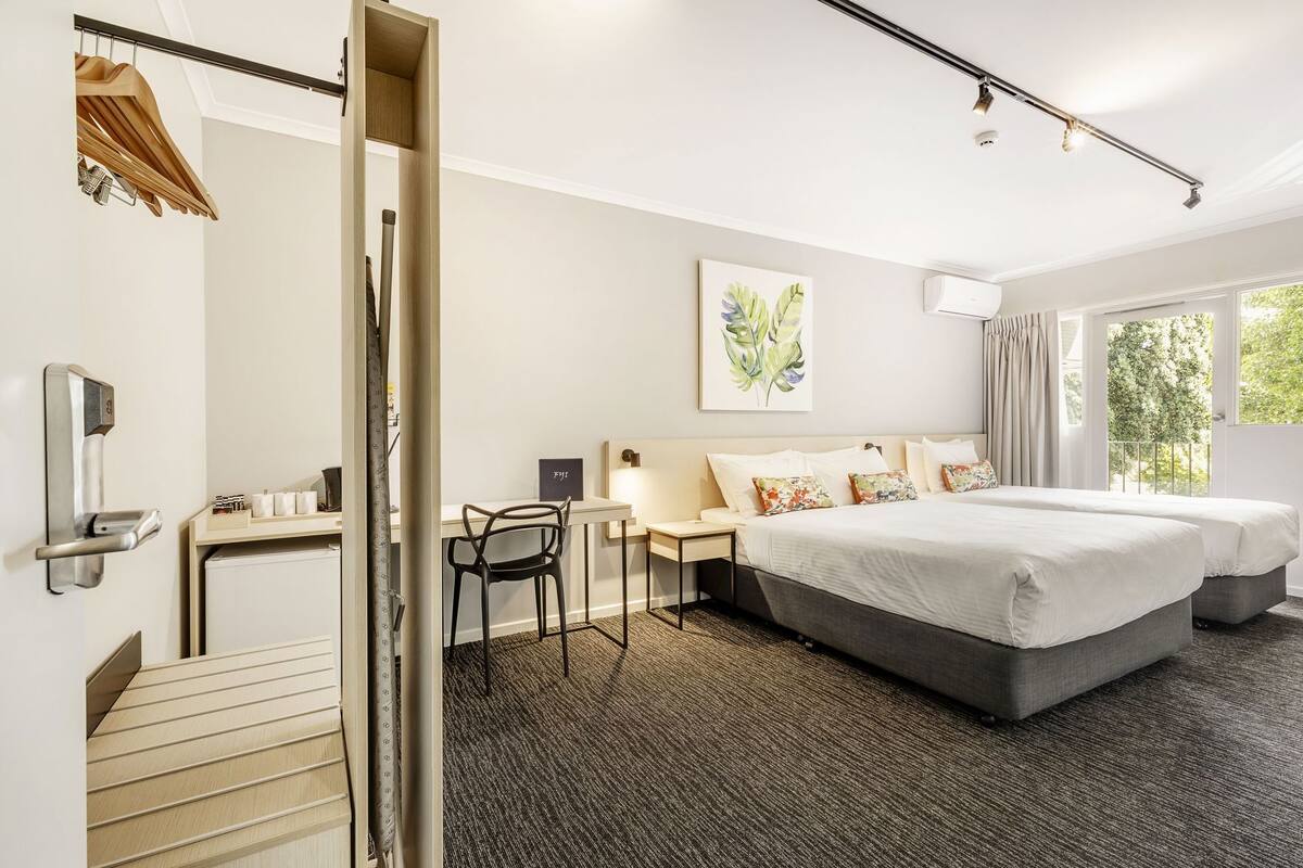 A hotel room with a bed, bedside tables, a desk, a chair, a wardrobe, and a window with a view.