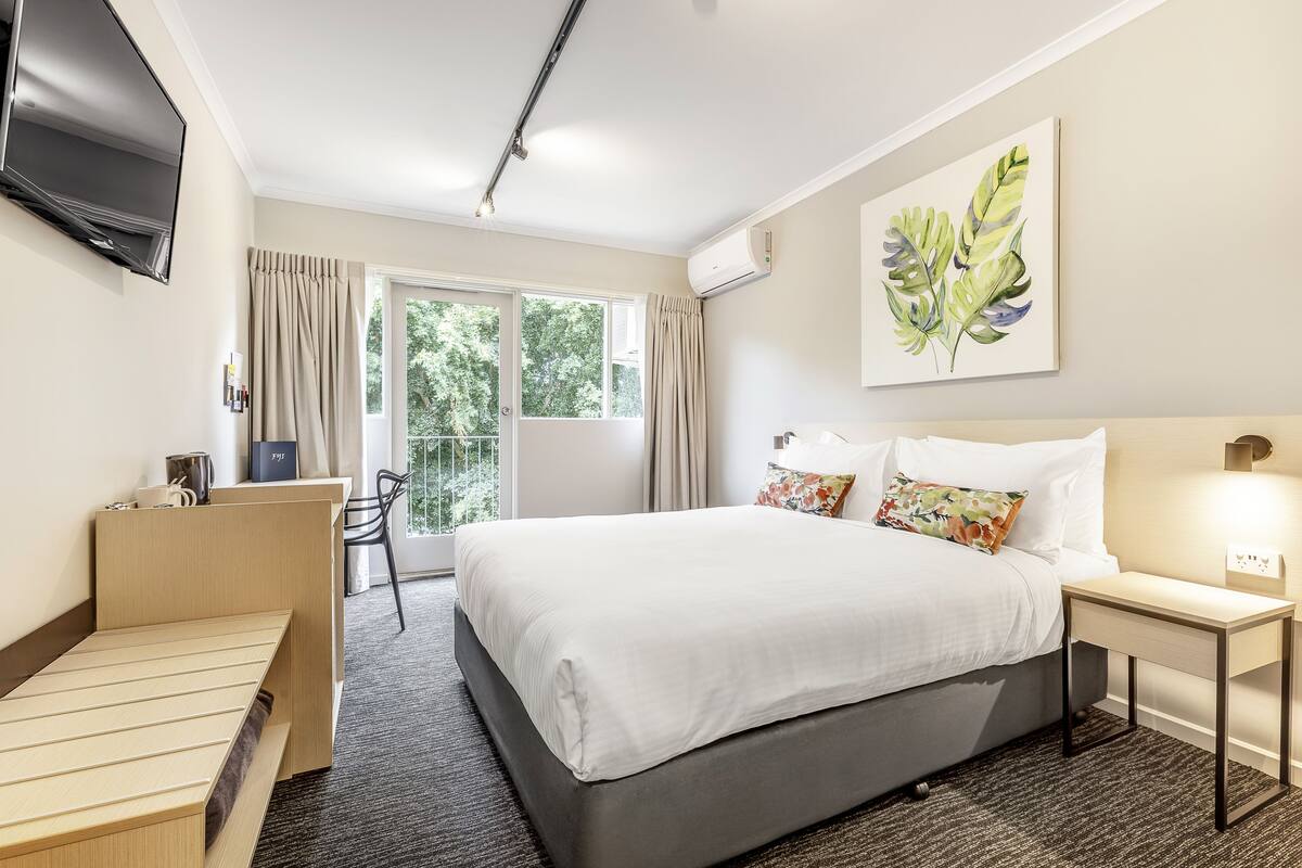 A hotel room with a bed, a desk, a chair, a television, and a window with curtains.