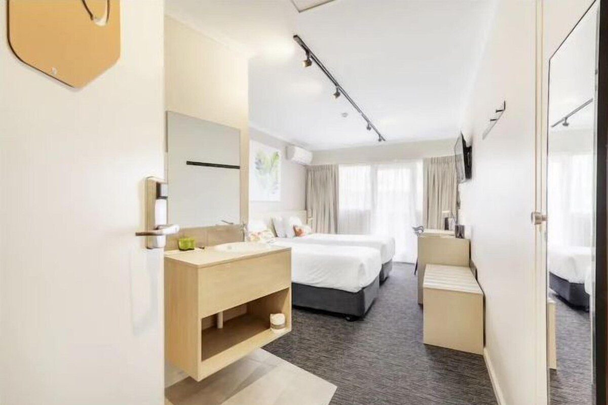 A hotel room with a bed, a bathroom with a sink and mirror, and a TV mounted on the wall.