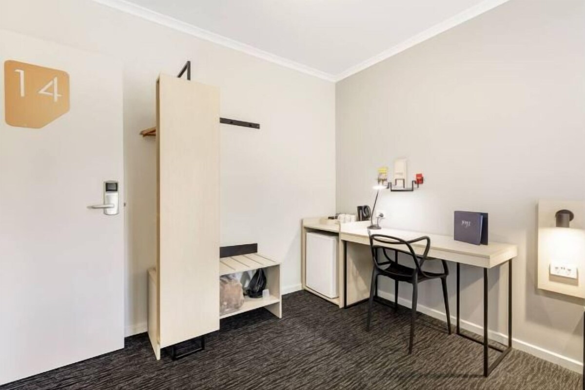 A hotel room with a desk, chair, and a small cabinet.
