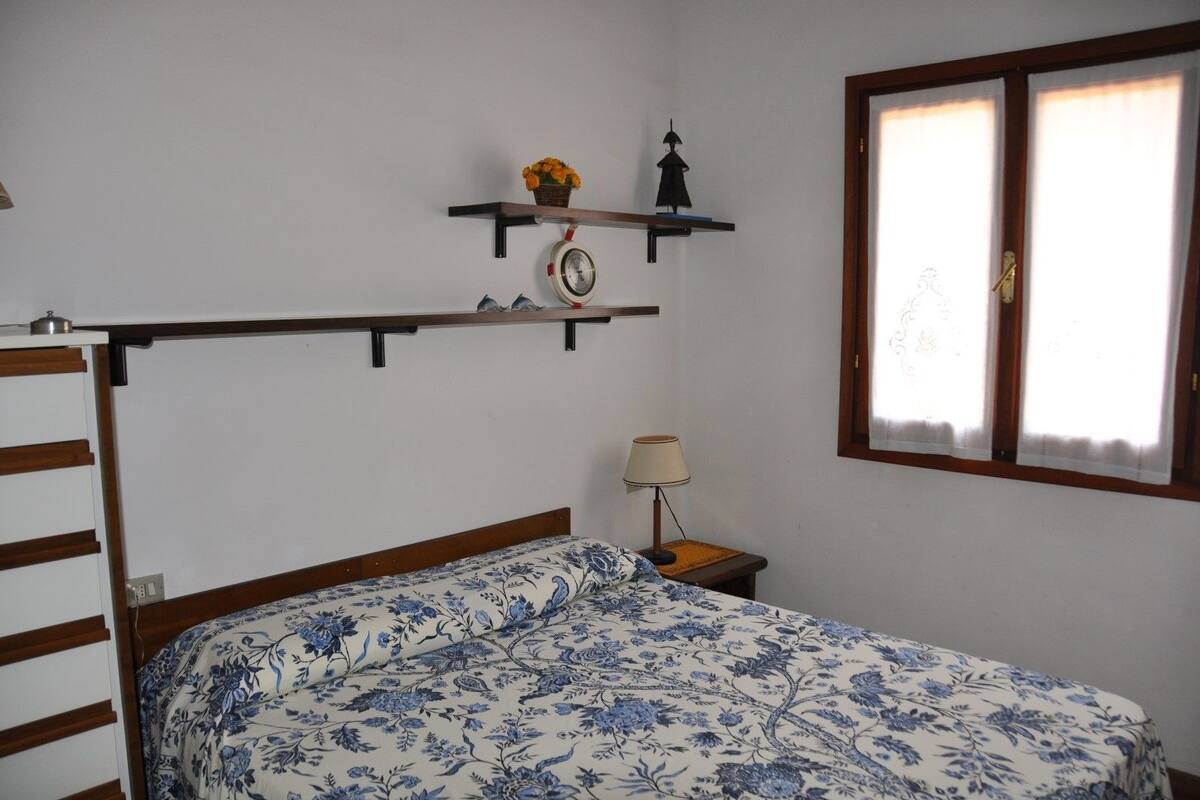 A bedroom with a bed, a nightstand, a lamp, a wall clock, and a window with curtains.