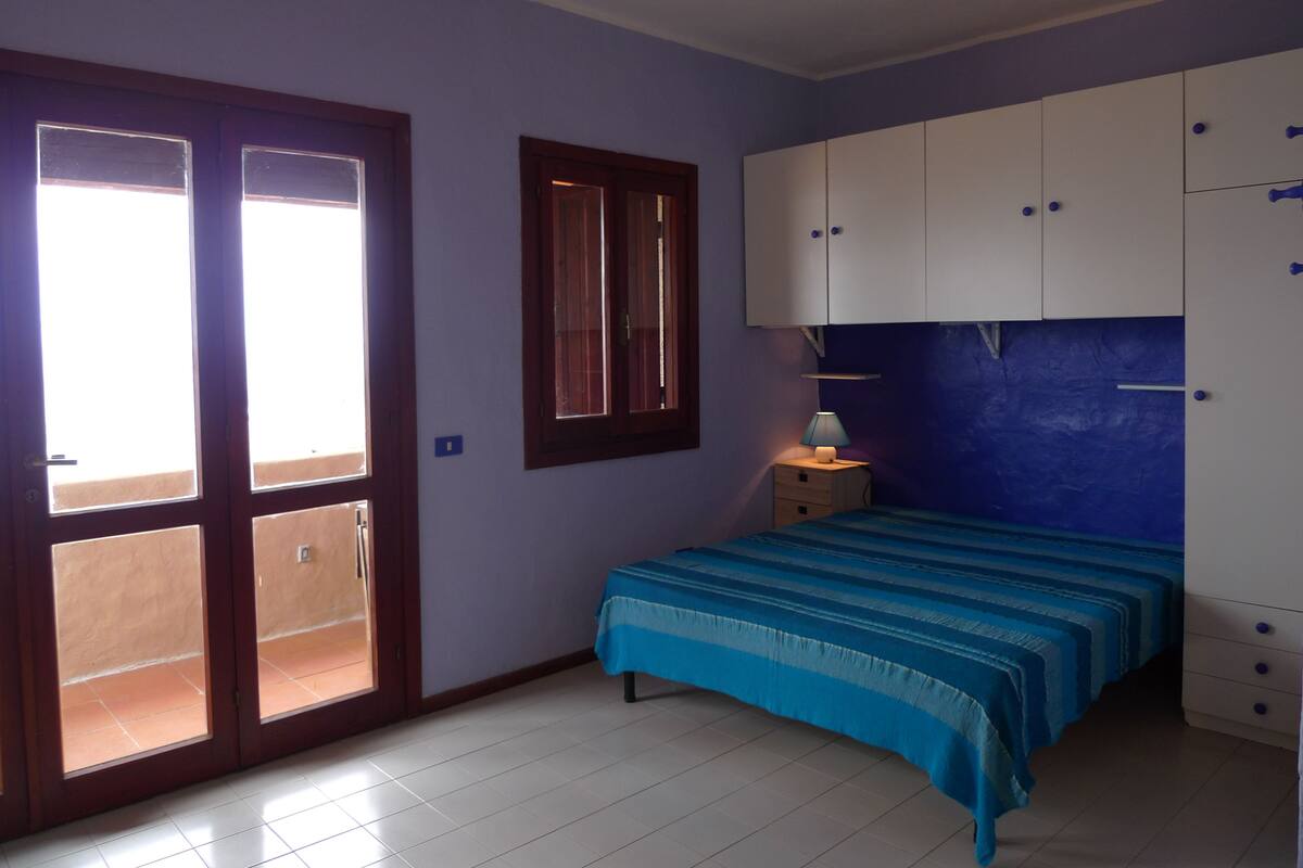 A bedroom with a bed, a wardrobe, a window, and a door.