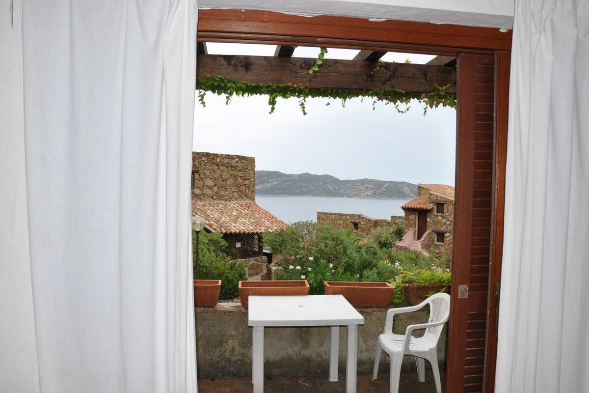 A patio with a white table and chair, a stone wall, and a view of the sea.
