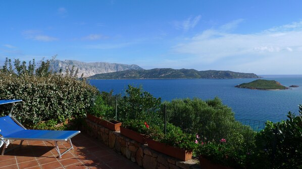 Una terraza con vista al mar, un muro de piedra y una silla azul.