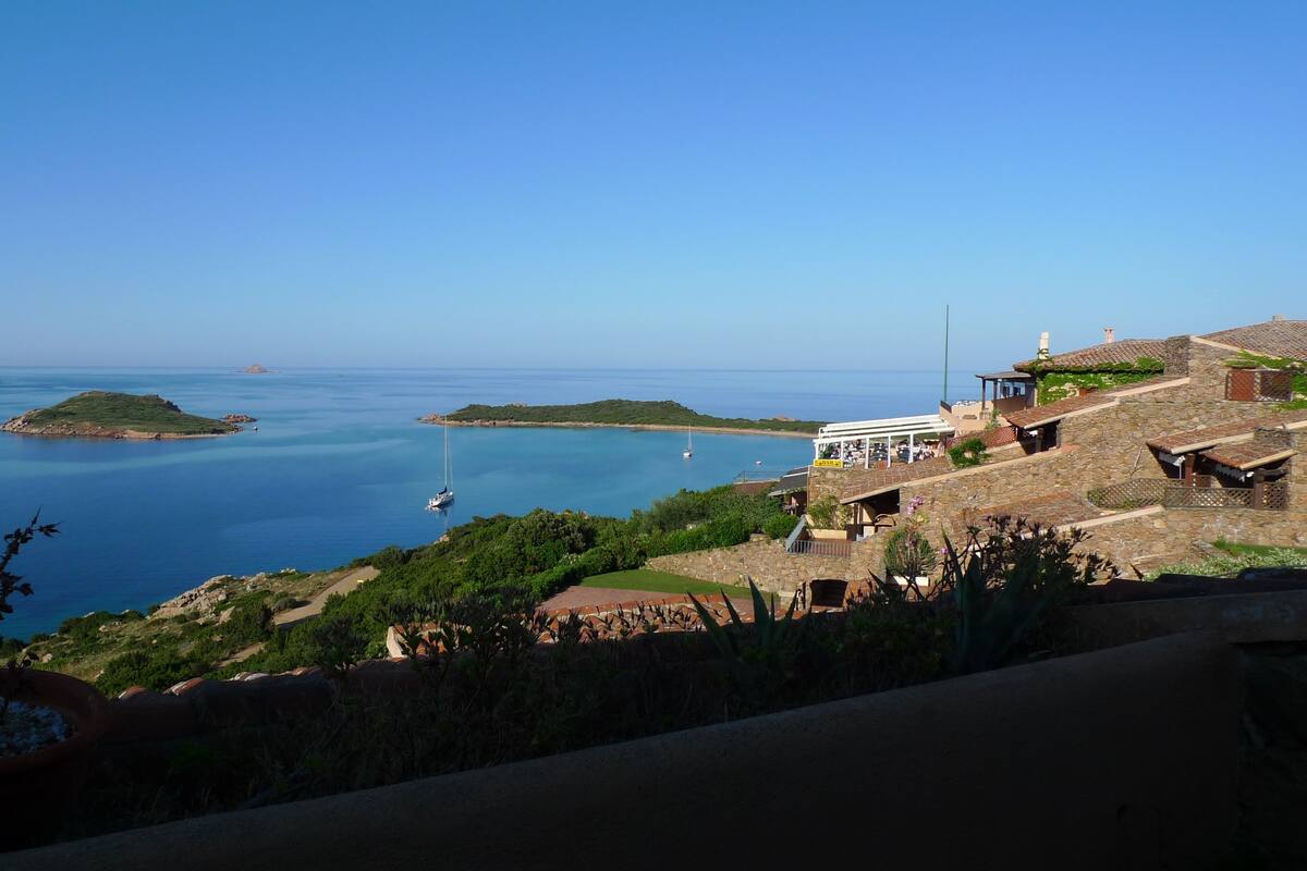 A coastal view with a stone building, a small island, and a clear blue sea.