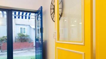 Un pasillo con una puerta amarilla, un reloj en la pared y vistas al exterior.