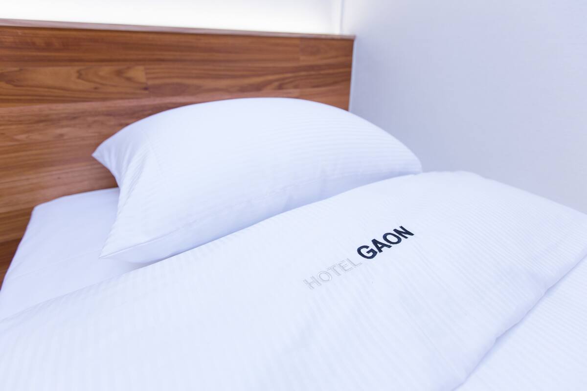 A neatly made bed with white bedding and a pillow labeled "HOTEL GAON".