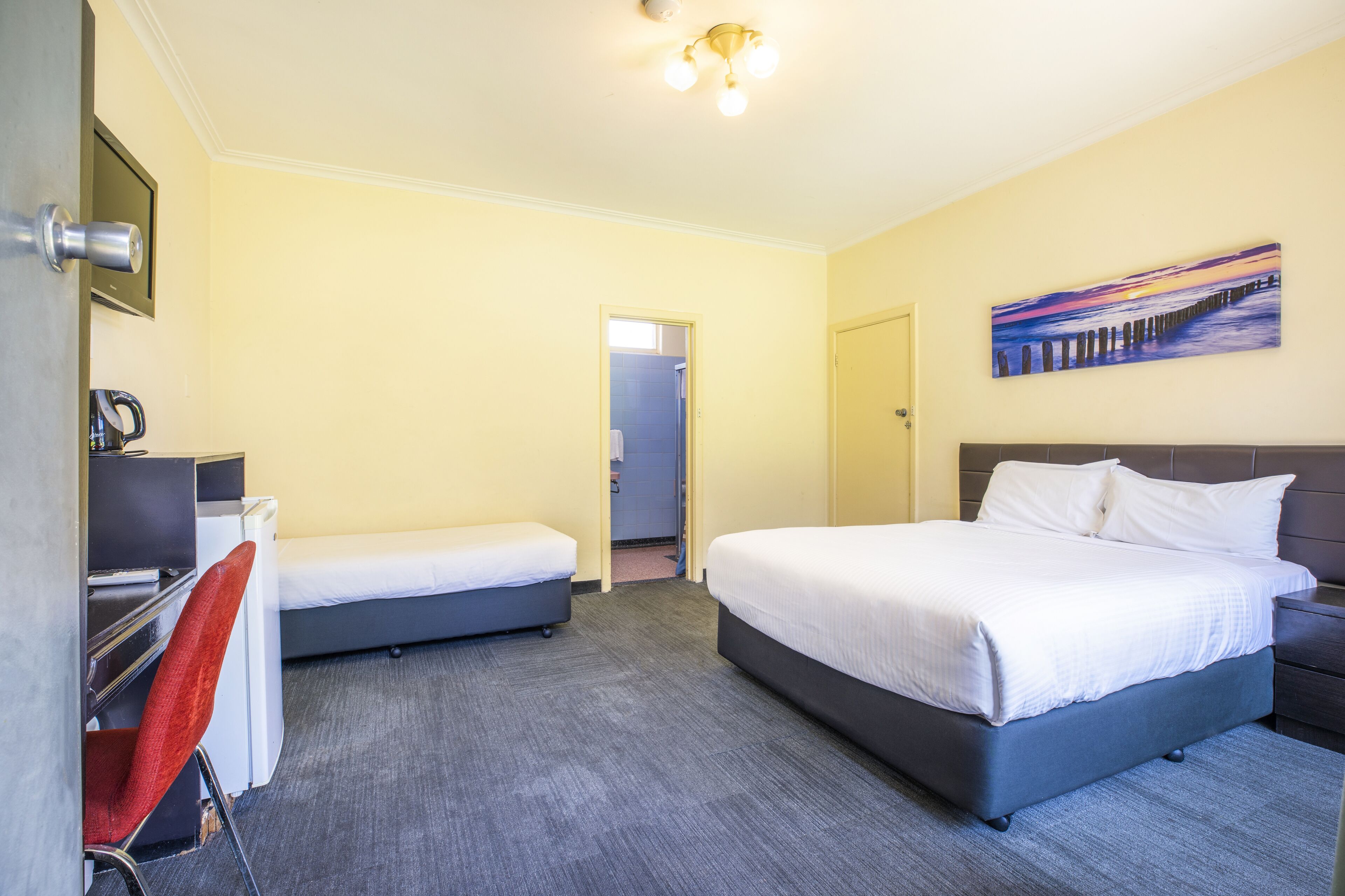 Una habitación de hotel con una cama grande, una cama más pequeña, un escritorio con una silla y un cuadro en la pared.
