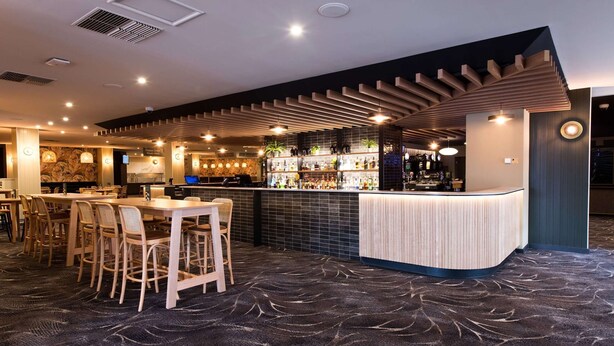 A bar area with a counter, seating, and a patterned carpet. - Links Hotel (Seaton)