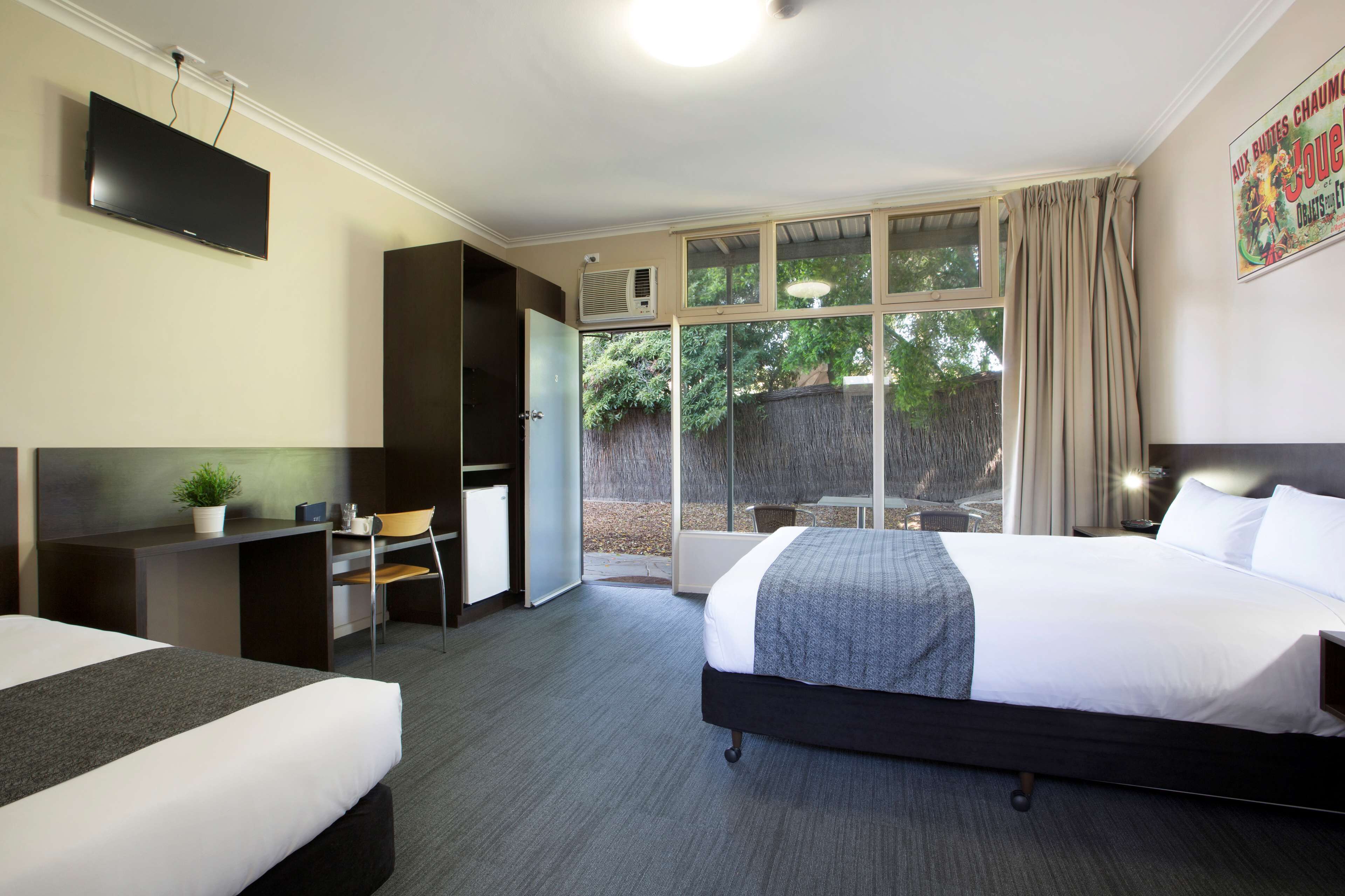 A hotel room with a bed, a desk, a chair, a TV, and a window with curtains.