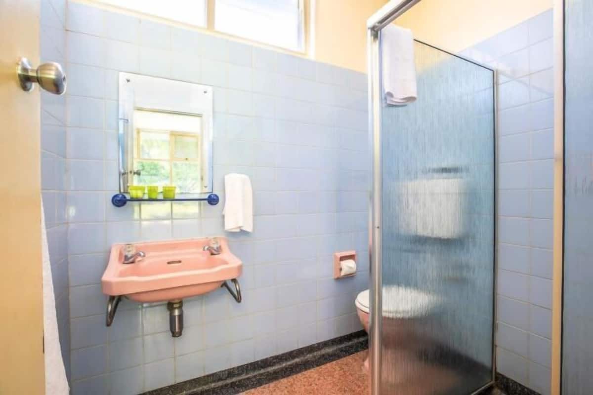 A bathroom with a pink sink, a toilet, a glass shower enclosure, and a window.