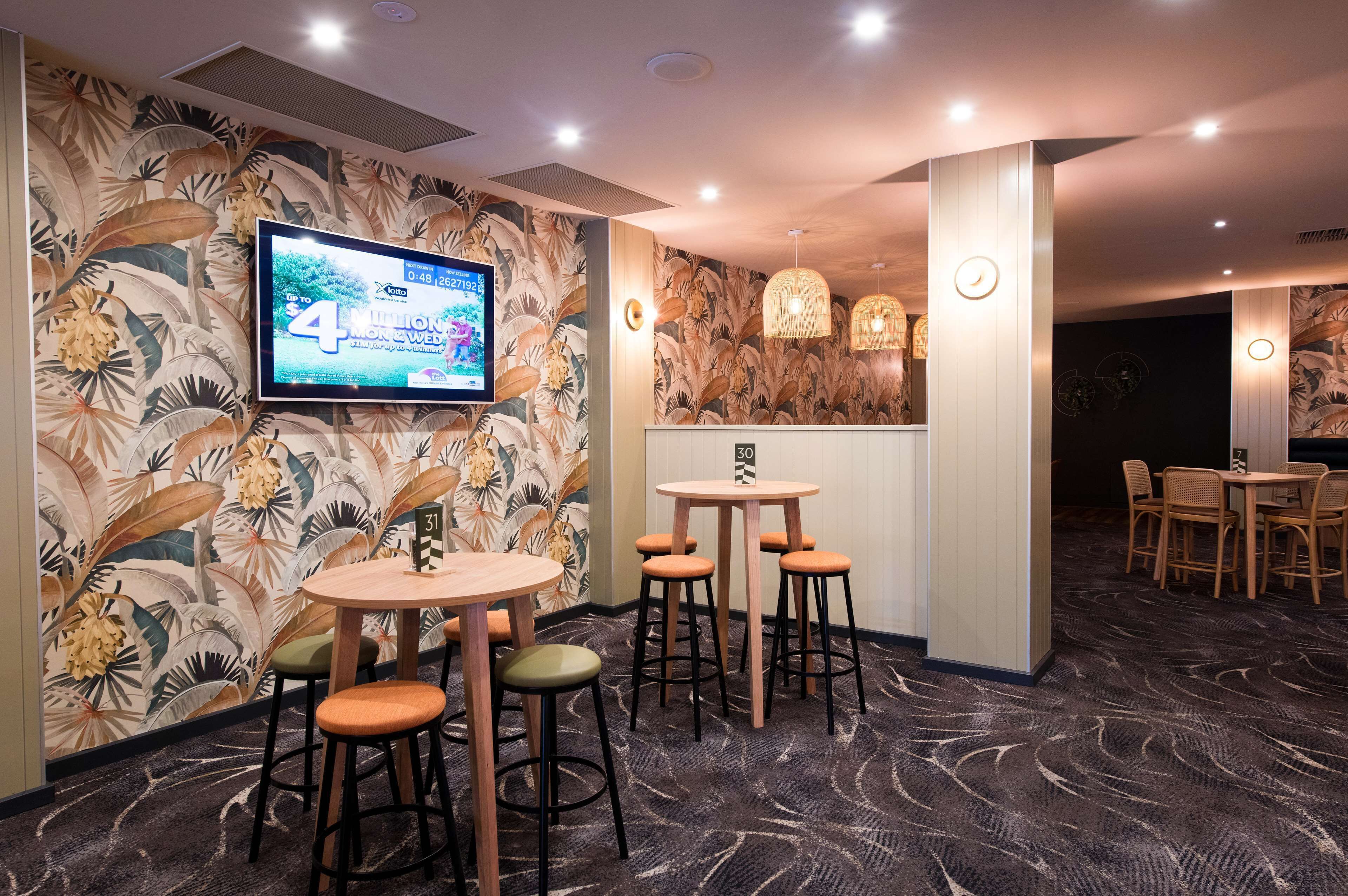 Zona de bar con pantalla de televisión, taburetes y pared con diseño.