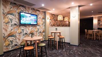Zona de bar con pantalla de televisión, taburetes y pared con diseño.