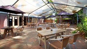 An outdoor patio area with tables and chairs, covered by a transparent roof, and umbrellas branded with "Carlton Dry". - Links Hotel (Seaton)