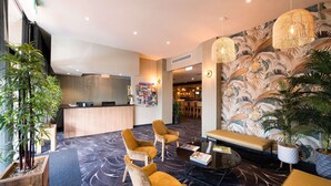 A hotel lobby with a reception desk, seating area, and a tropical-themed wall. - Links Hotel (Seaton)