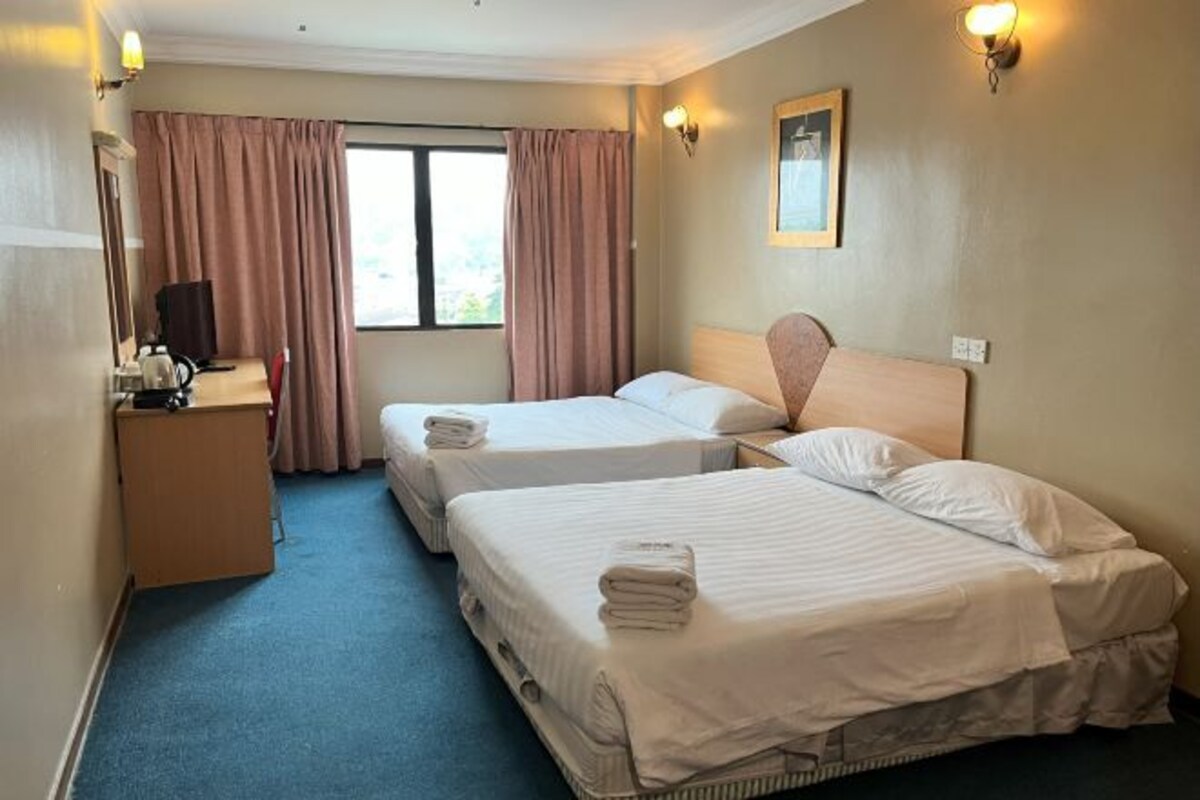 A hotel room with two beds, a desk with a chair, a television, and a window with curtains.