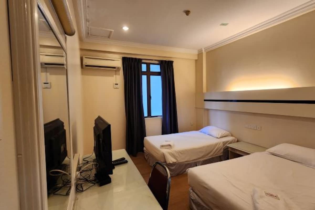 Habitación de hotel con dos camas, un escritorio con computadora y aire acondicionado.