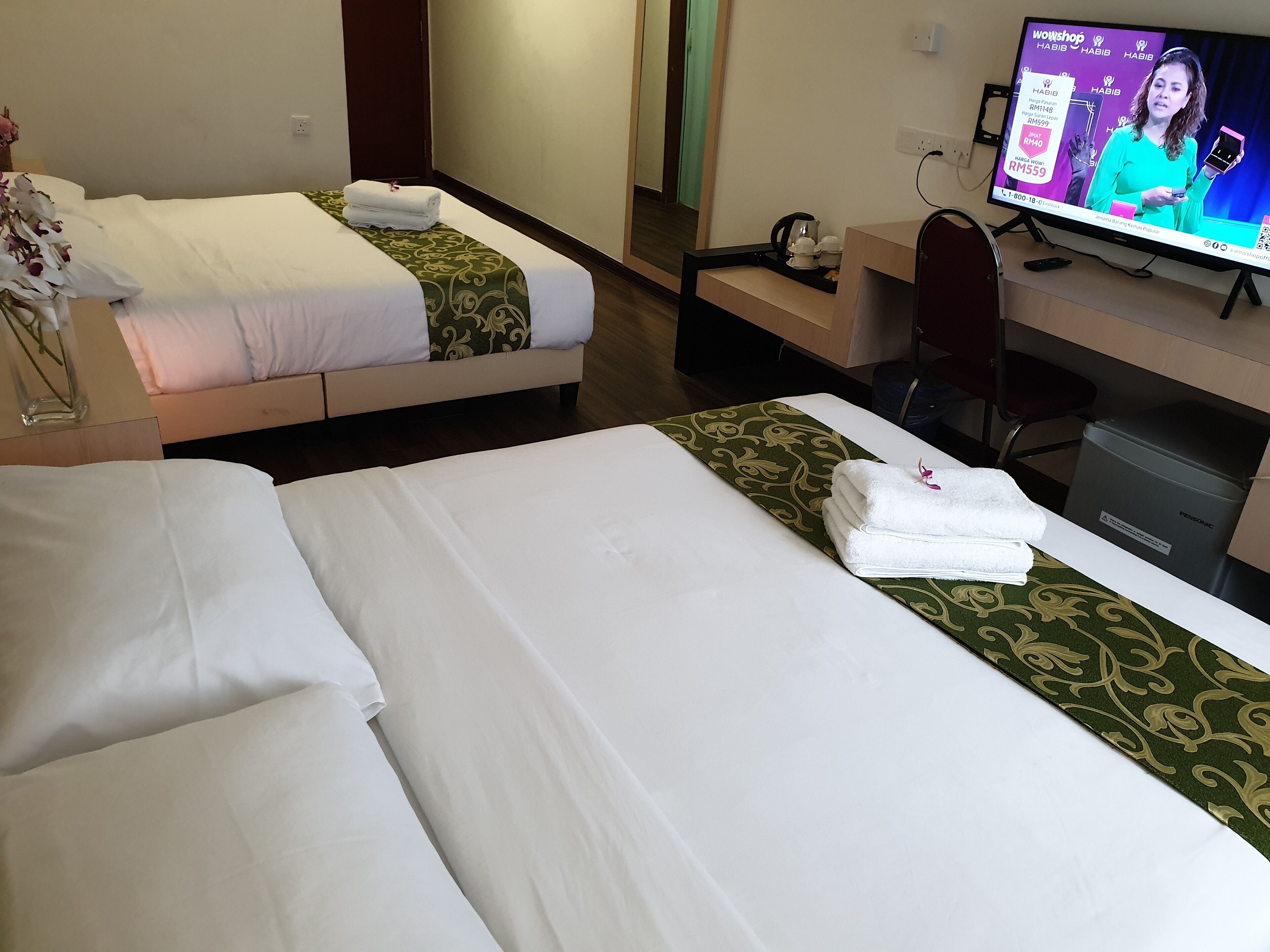 A hotel room with two beds, a desk, a television, and a trash bin.