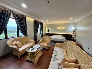 A hotel room with a bed, two wicker chairs, a small table with a remote control, and a view of the outdoors through large windows. - Fair Park Hotel (Ipoh)