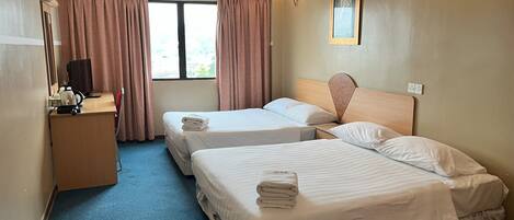 A hotel room with two beds, a desk with a kettle, a chair, and a window with curtains.