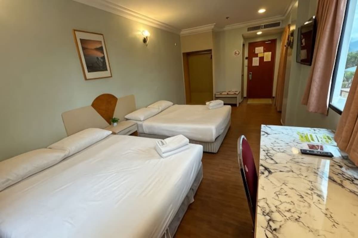 Habitación de hotel con dos camas individuales, una mesita de mármol, una silla, una mesita de noche y una puerta que da a otra habitación.
