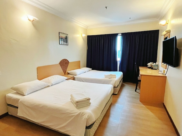 Habitación de hotel con dos camas, un escritorio, una televisión y una ventana con cortinas.
