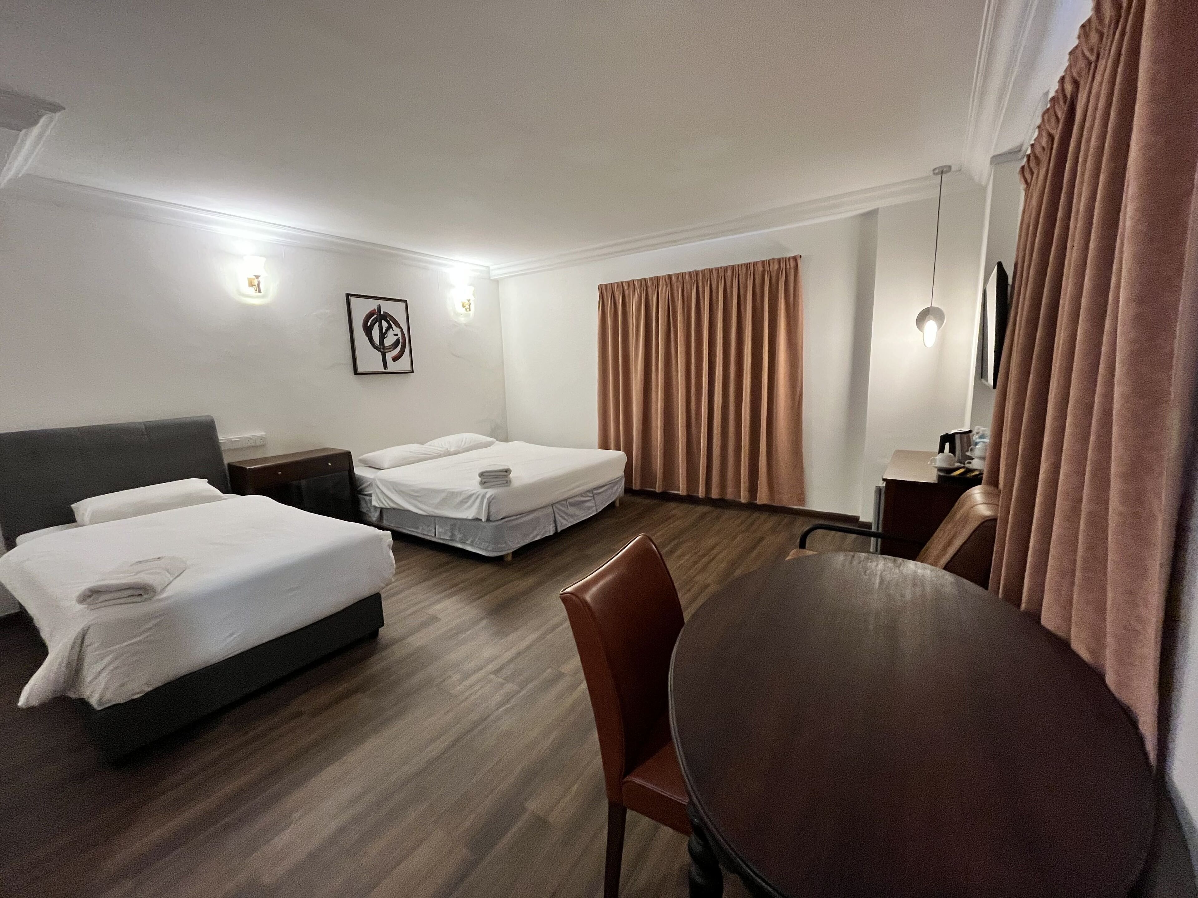 A hotel room with two beds, a dining table, a desk, and a large window with curtains.